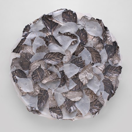 round wall hung artwork consisting of randomly stacked and overlapping beech leaves made in milky white plastic aged silver and roughly textured aluminium